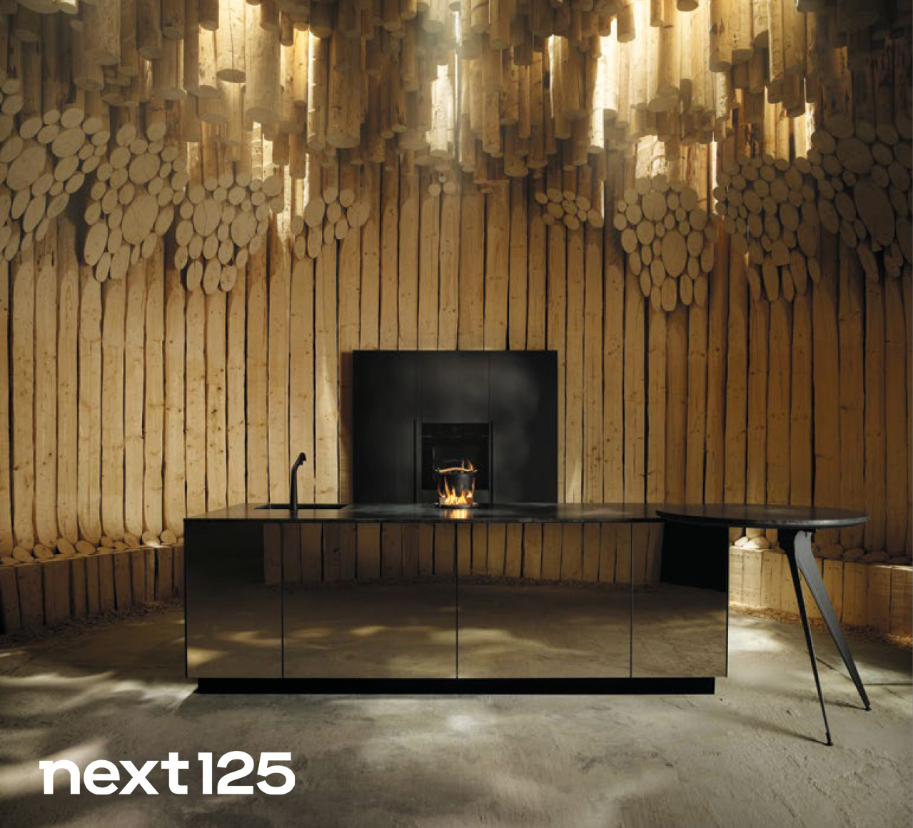 Next125 Küchen bei Himmlisch Wohnen Moderne schwarze Kücheninsel vor Holzverkleidung mit integriertem Kamin