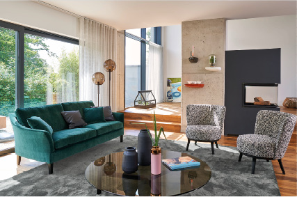 Möbel bei Himmlisch Wohnen Wohnzimmer mit grünem Sofa, Kaminwand und großen Fenstern