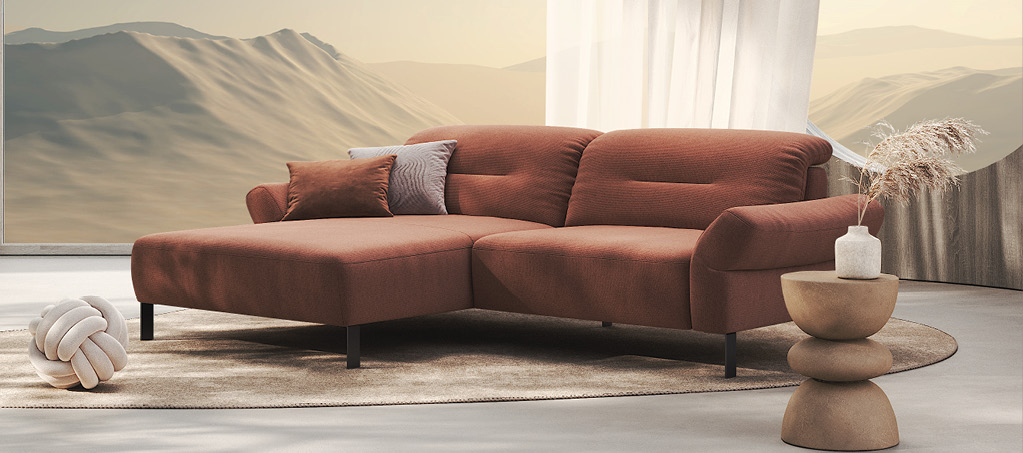 Rostfarbenes Ecksofa mit Kissen vor Panoramafenster mit Bergblick.