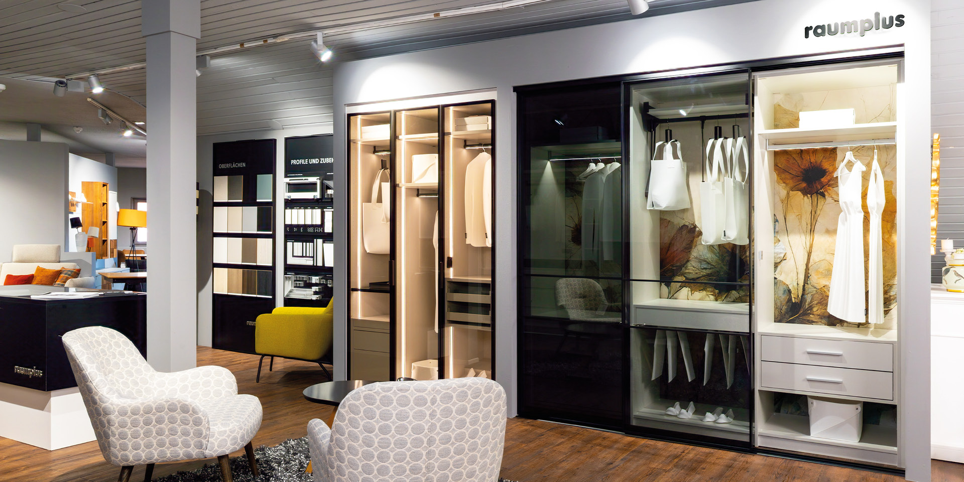 Möbelausstellung mit beleuchteten Schiebetür-Kleiderschränken und Sitzgruppe.