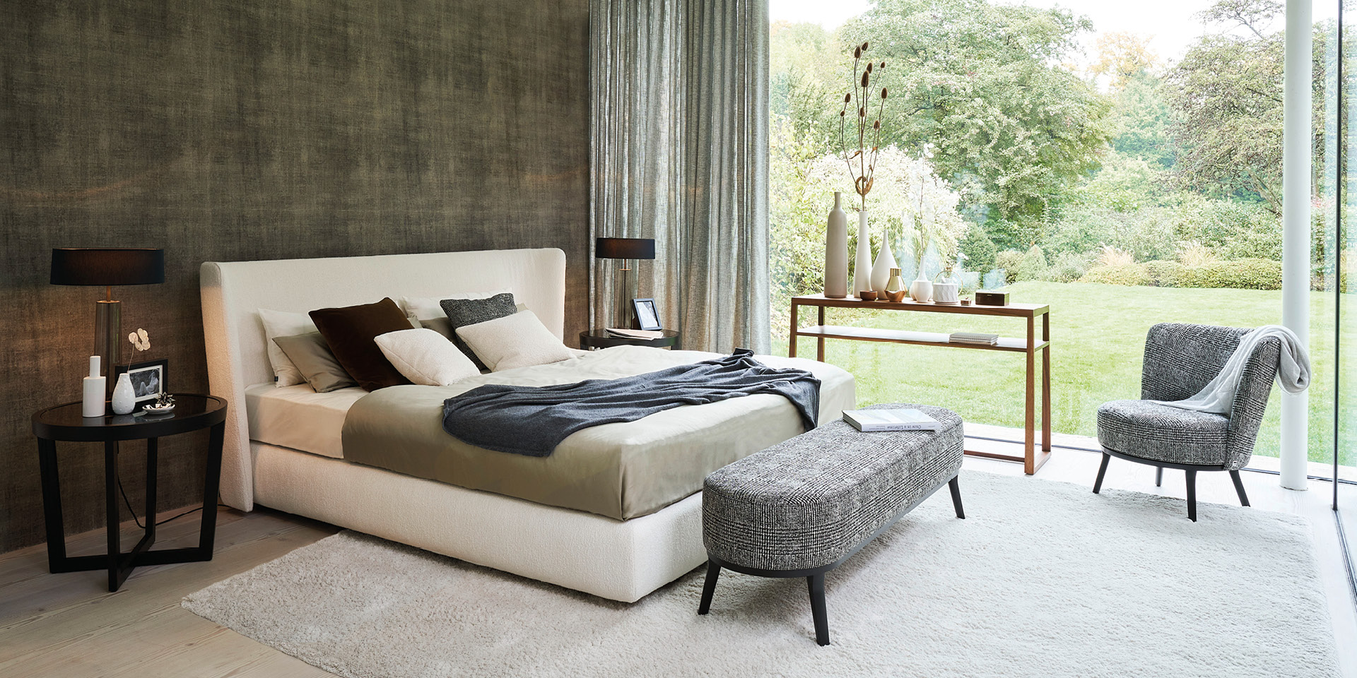 Modernes Schlafzimmer mit Polsterbett, Bank am Fußende und Gartenblick.