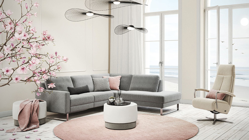 Helles Wohnzimmer mit grauem Ecksofa, Sessel und Meerblick.