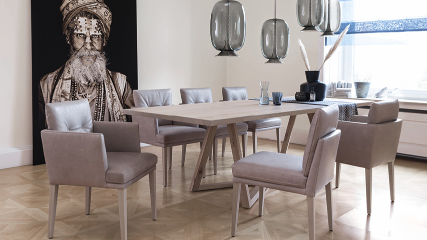 Esszimmer mit Holztisch, Polsterstühlen, Pendelleuchten und großem Porträtbild.