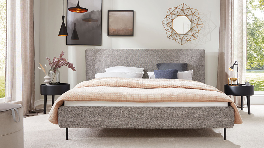 Modernes Schlafzimmer mit grauem Polsterbett, Nachttischen und Wanddeko.