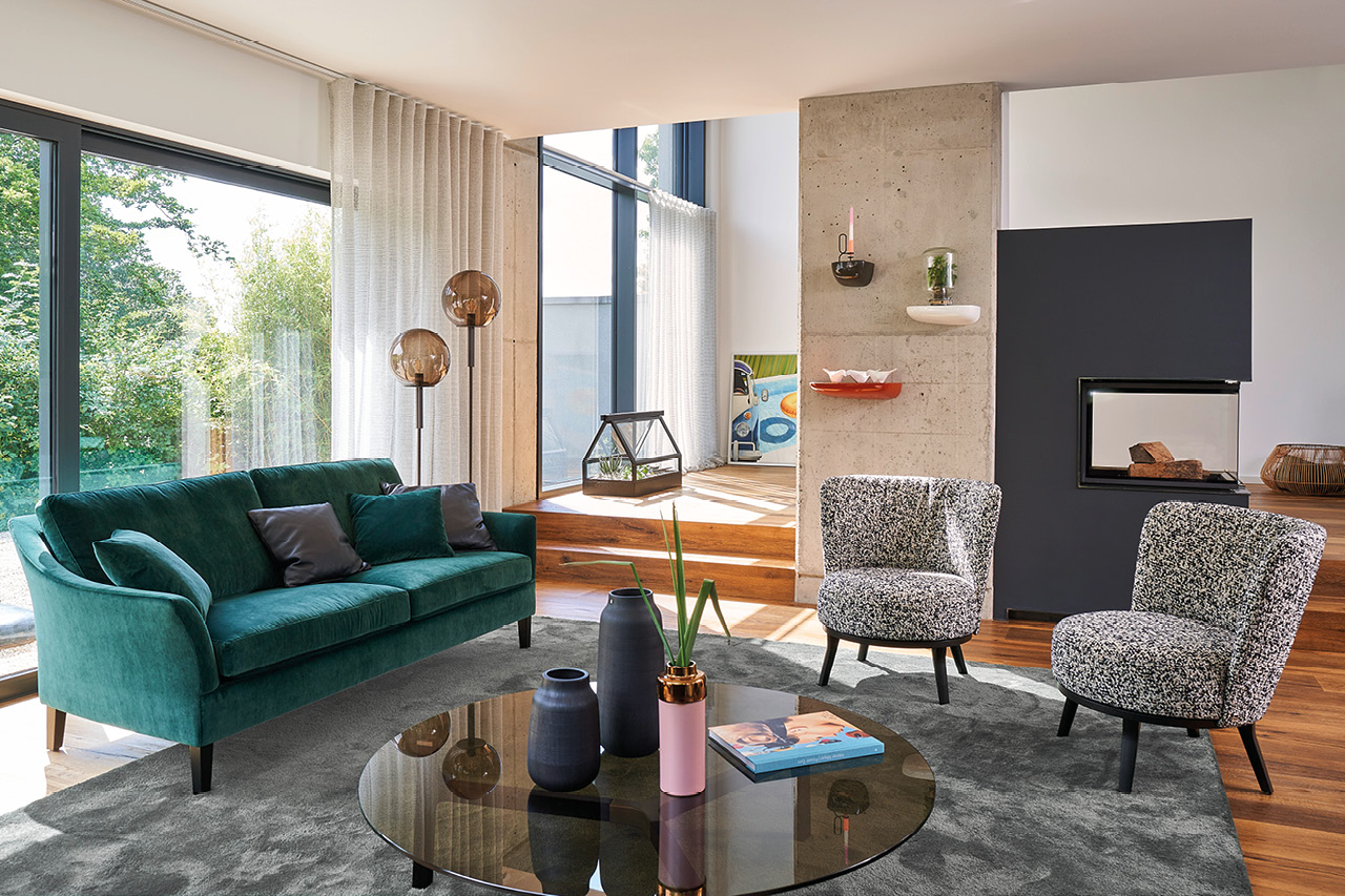 Modernes Wohnzimmer mit grünem Sofa, zwei Sesseln und Kamin.