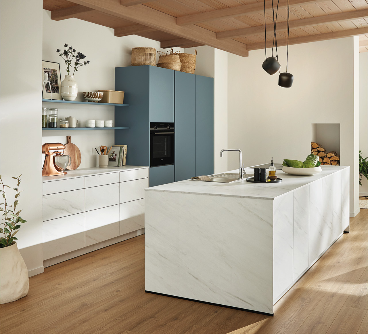 Offene Küche mit blauem Hochschrank, weißer Insel in Marmoroptik und Spüle.