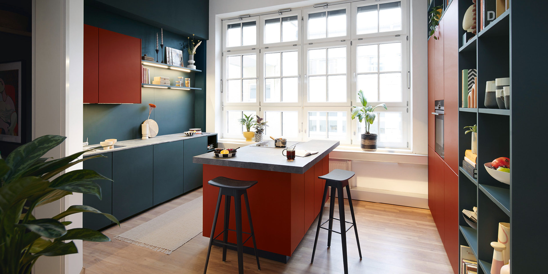 Farbige Küche mit roter Kochinsel, Barhockern und großen Fenstern.