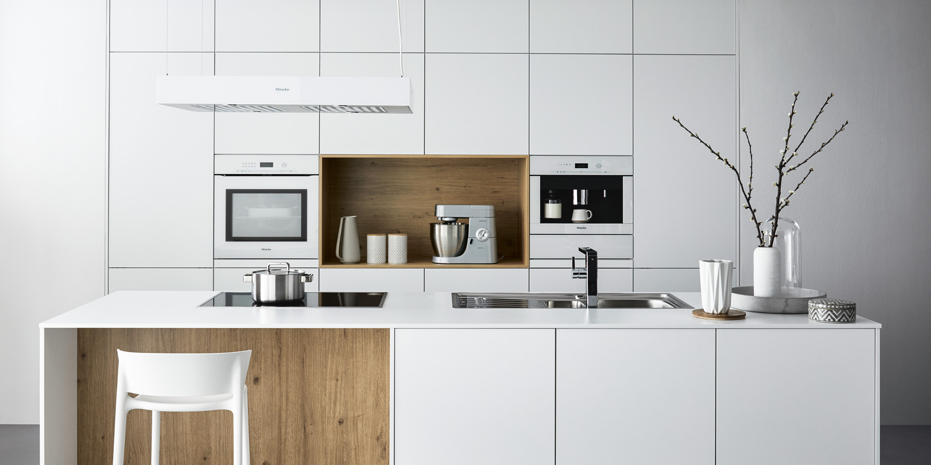 Weiße Küche mit Holz-Nische, Kochinsel, Spüle und Induktionsfeld.