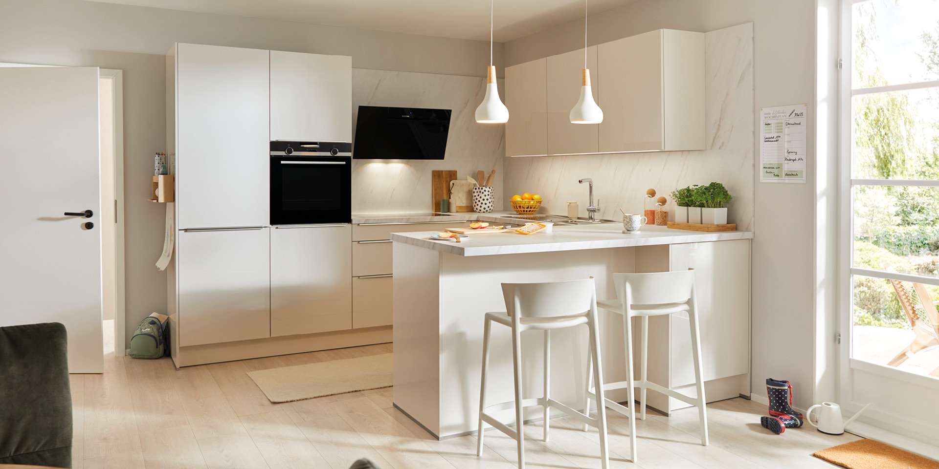 Helle Wohnküche mit Kochinsel, Barhockern, Einbaugeräten und Pendelleuchten