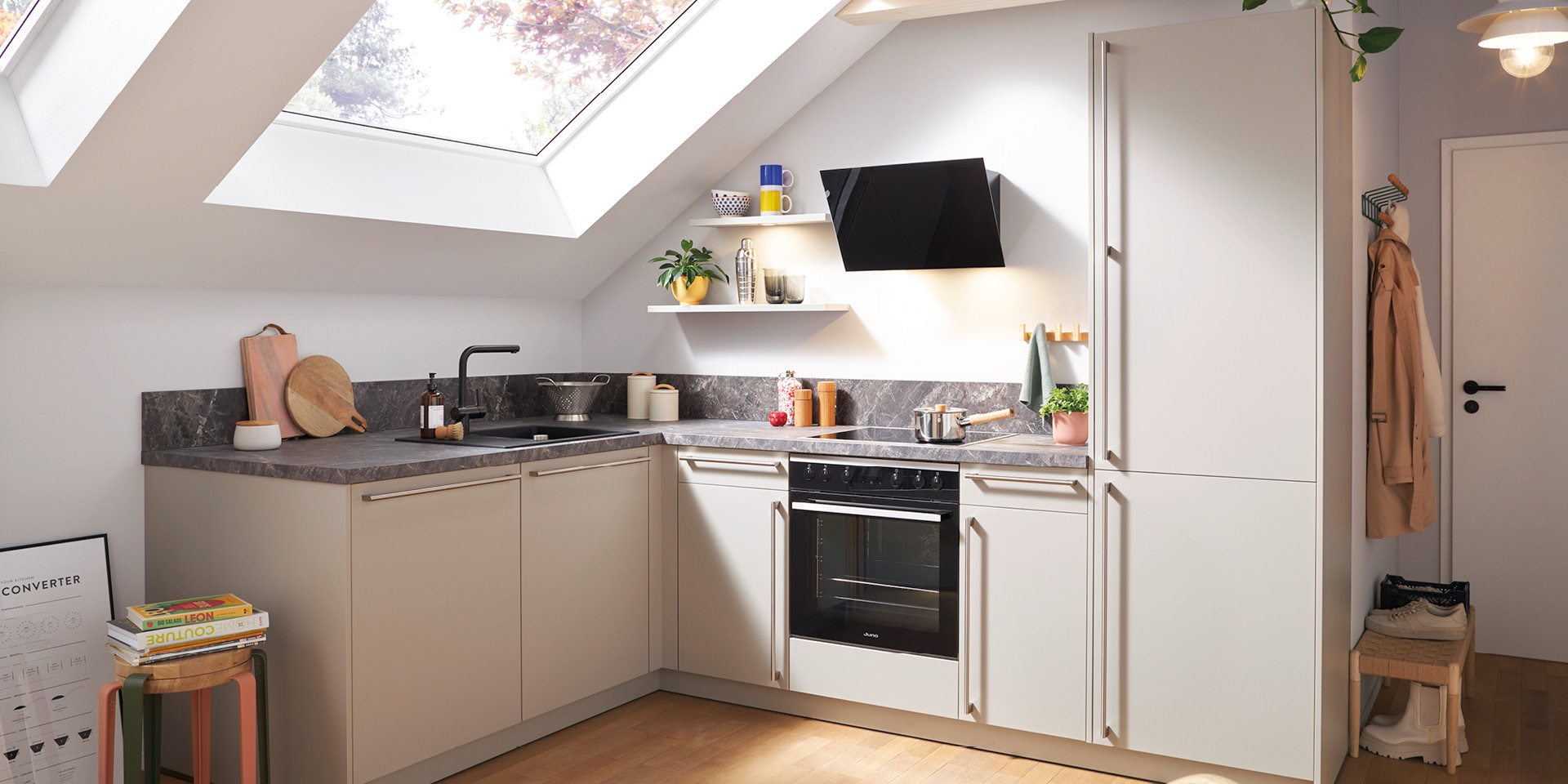 Moderne Dachschrägenküche mit Oberlicht, beigen Fronten, schwarzer Spüle und Ofen.