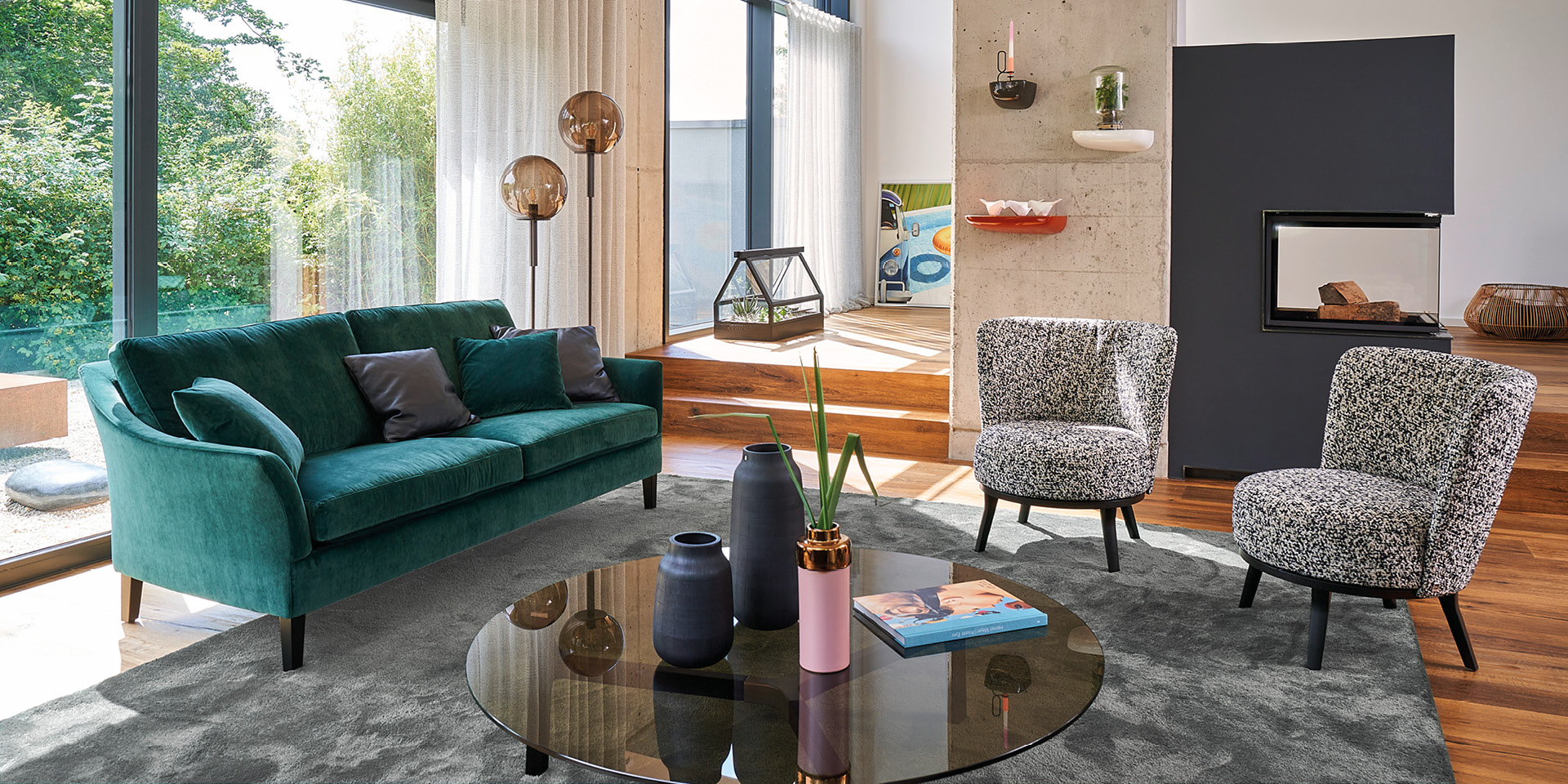 Wohnzimmer mit grünem Sofa, zwei Sesseln und rundem Couchtisch