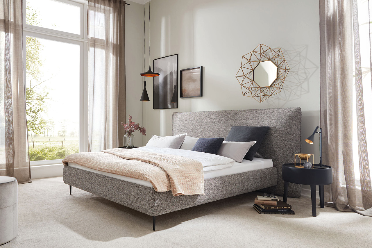 Helles Schlafzimmer mit grauem Polsterbett, Nachttisch und Wandspiegel