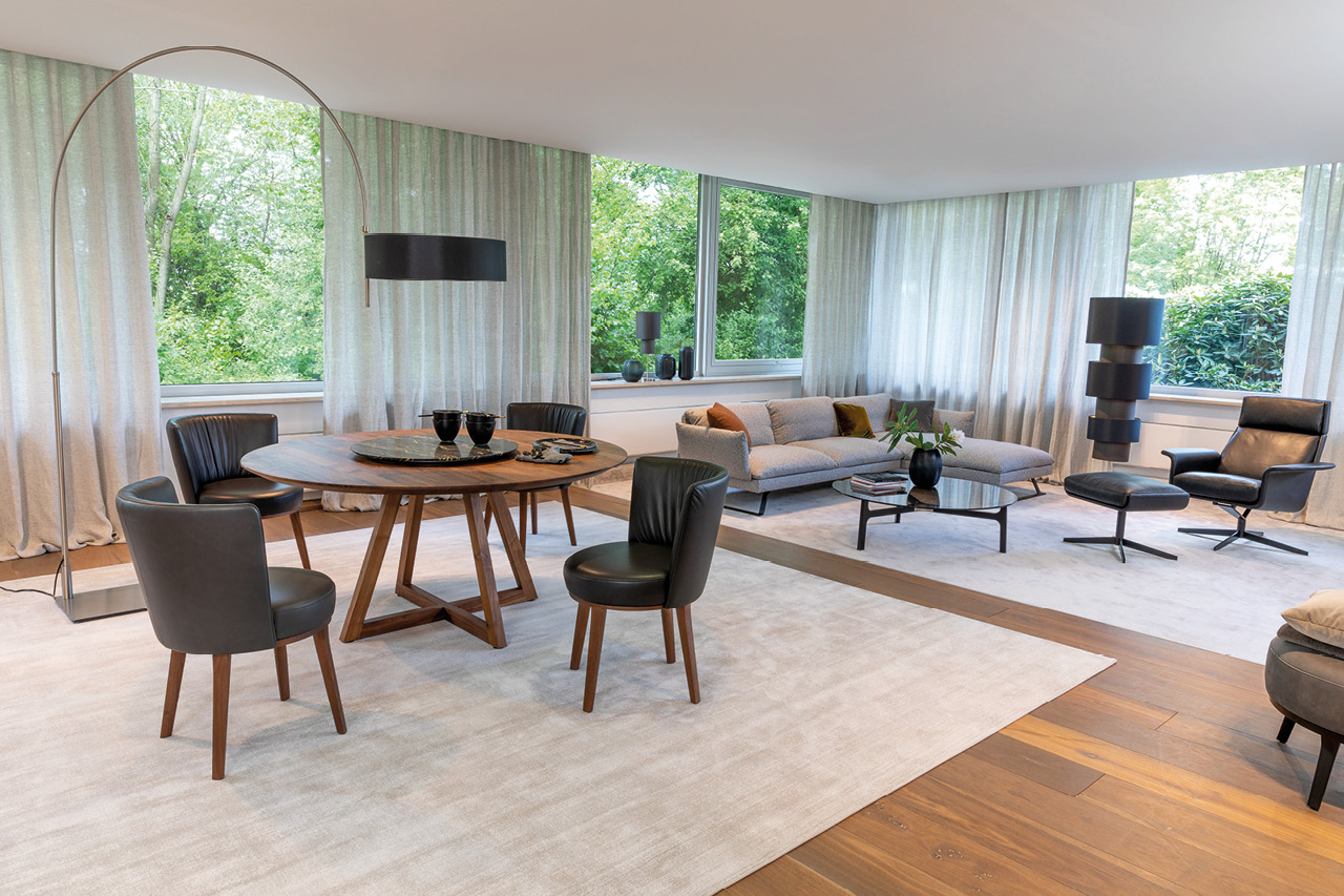 Offener Wohn-Essbereich mit rundem Holztisch, Stühlen, Sofa und großen Fenstern