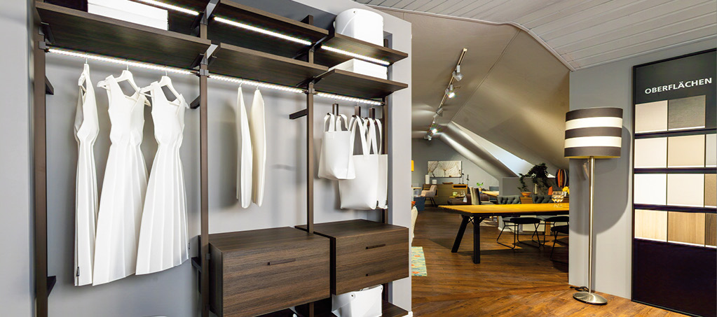 Offenes Schranksystem mit Kleiderstange, Regalböden und Holzschubladen im Showroom.