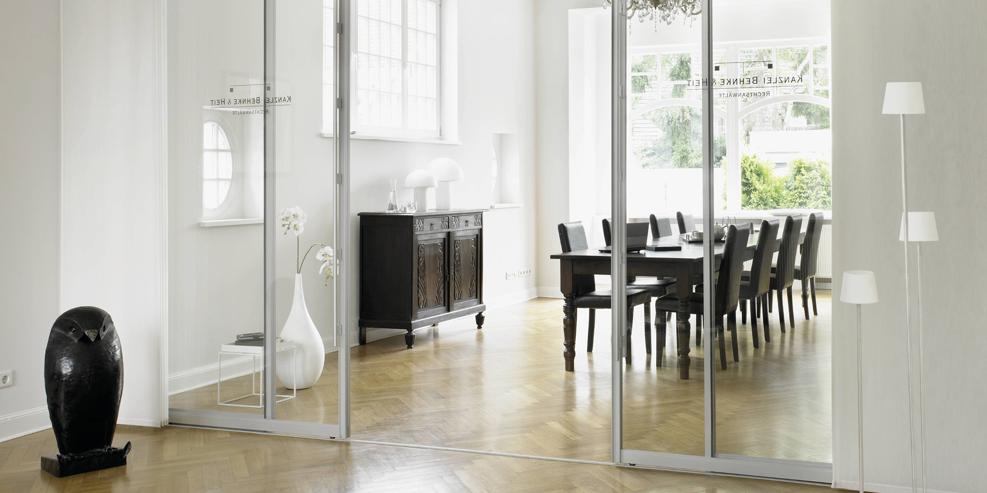 Glas-Schiebetüren als Raumteiler vor Essbereich mit großem Tisch.