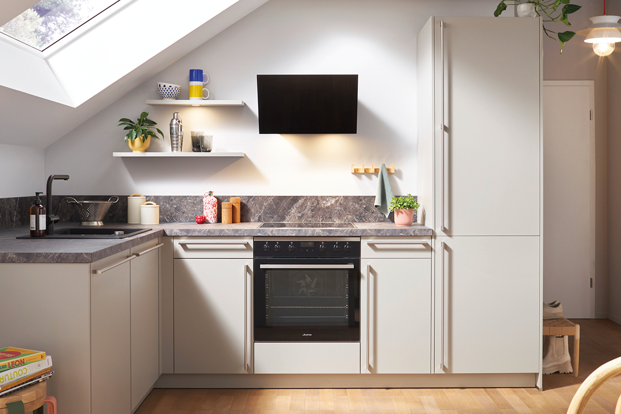 Moderne Dachschrägenküche mit Oberlicht, beigen Fronten, schwarzer Spüle und Ofen.