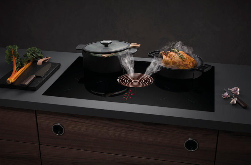 Kochfeldabzug saugt Dampf zwischen Topf und Bräter auf Kücheninsel ab