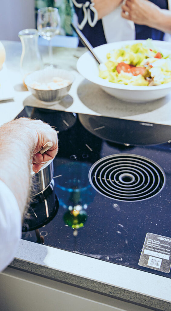 Person kocht am Kochfeld mit integriertem Dunstabzug am Esstisch