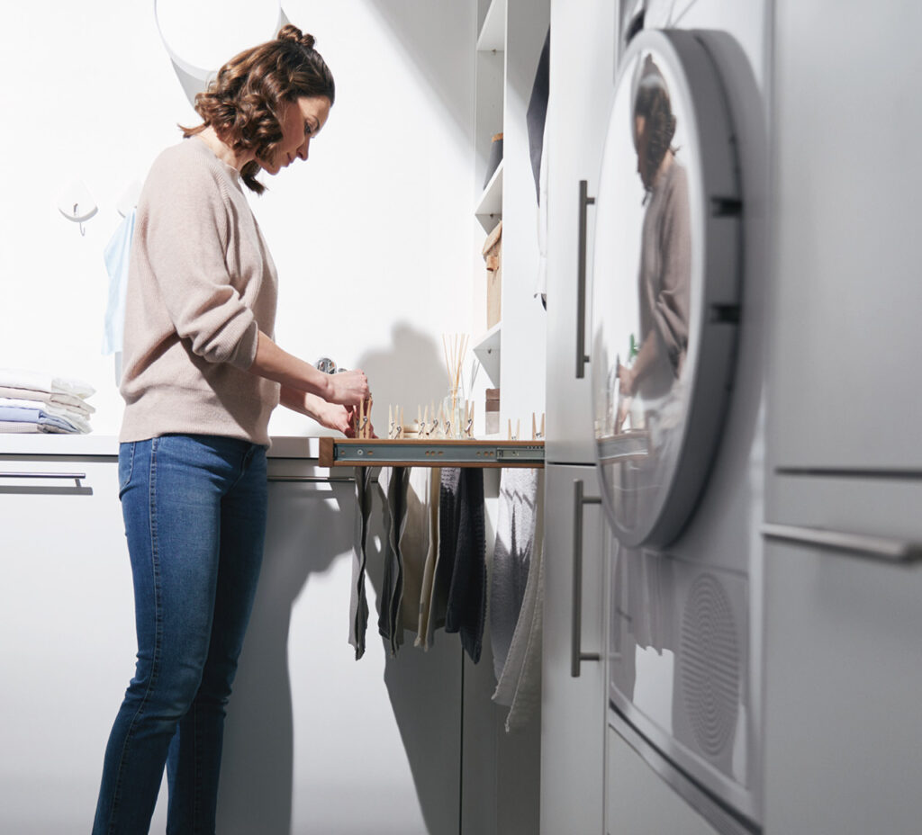 Frau sortiert Wäsche im Hauswirtschaftsraum neben Waschmaschine und Schränken.