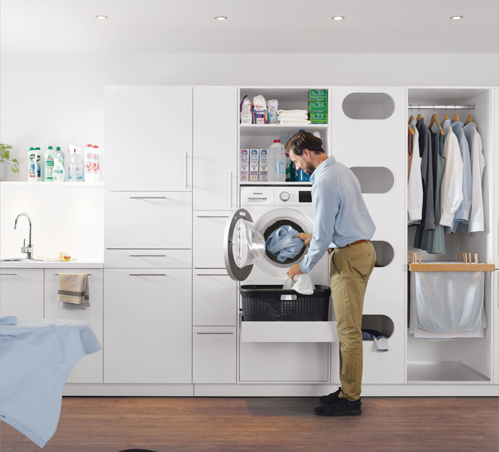 Mann lädt Wäsche in Waschmaschine im modernen Hauswirtschaftsraum.
