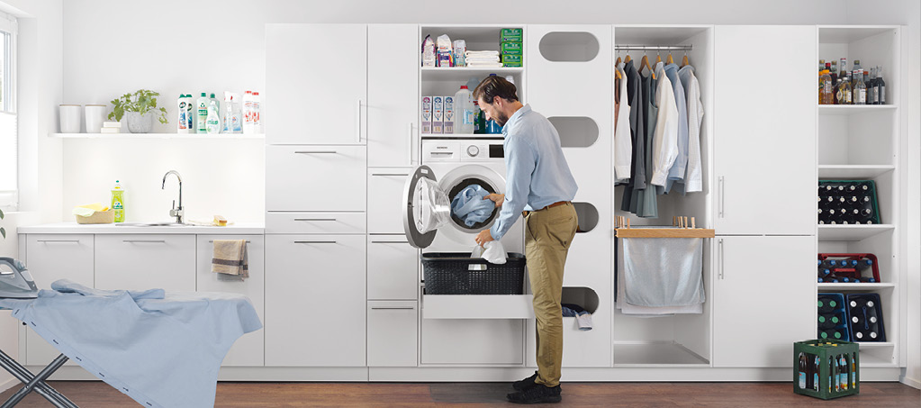 Mann lädt Wäsche in Waschmaschine im modernen Hauswirtschaftsraum.