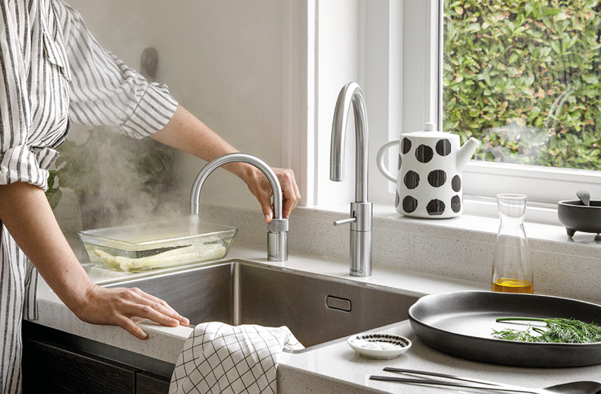 Dampfende Schüssel in Spüle neben zwei Küchenwasserhähnen am Fenster