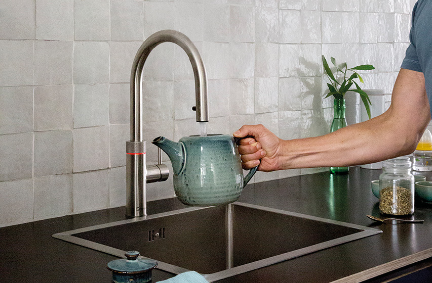 Hand füllt Teekanne am hohen Küchenwasserhahn über Edelstahlspüle