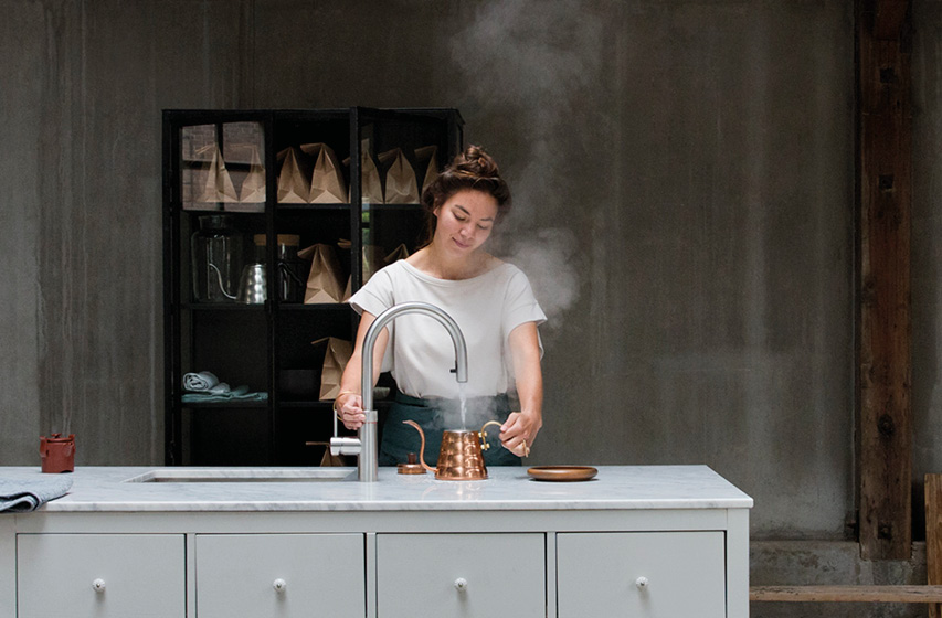Person füllt dampfendes Wasser am Küchenwasserhahn auf Kücheninsel