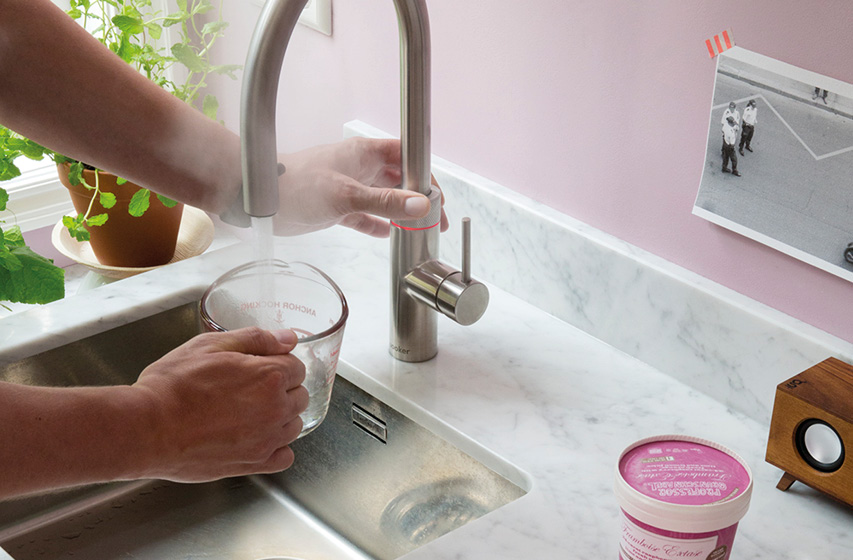 Hand füllt Messbecher am Küchenwasserhahn über Edelstahlspüle