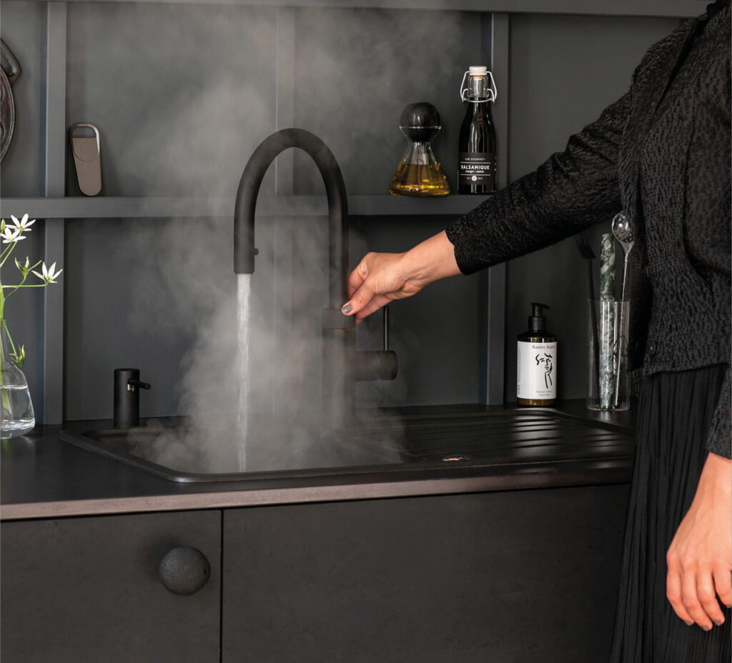 Hand bedient schwarzen Küchenwasserhahn über dunkler Spüle mit Wasserdampf