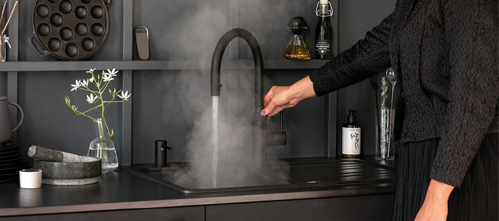 Hand bedient schwarzen Küchenwasserhahn über dunkler Spüle mit Wasserdampf