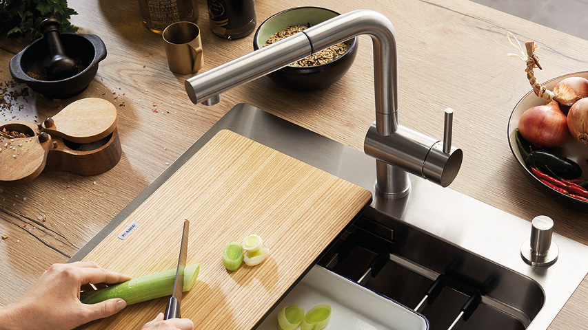 Schneidebrett über Küchenspüle mit Edelstahlhahn, Lauch wird geschnitten