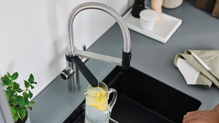 Wasserhahn mit Brause füllt Glas mit Zitronenwasser über schwarzer Spüle