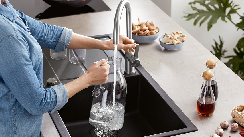 Person füllt Wasserkaraffe am Küchenwasserhahn über schwarzer Spüle