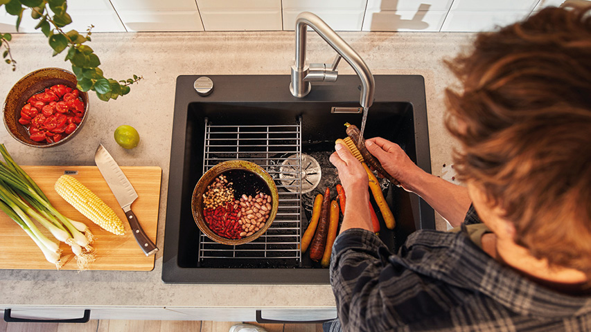 Person wäscht Gemüse in schwarzer Küchenspüle unter Edelstahlhahn