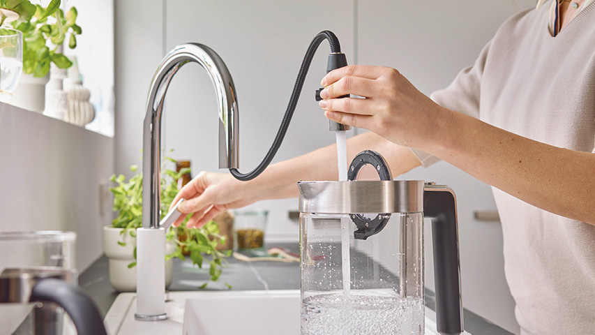 Person füllt Wasserbehälter an Küchenarmatur mit ausziehbarer Brause