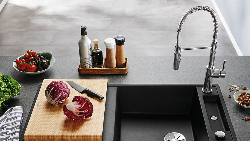 Schwarze Küchenspüle mit Federhahn neben Schneidebrett und Gemüse