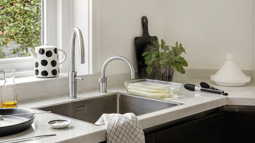 Edelstahlspüle mit zwei Küchenarmaturen auf heller Arbeitsplatte am Fenster