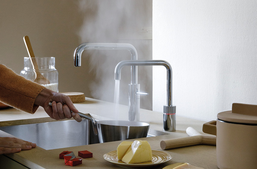 Kochendes Wasser aus Quooker Hahn füllt Topf, Dampf steigt auf.