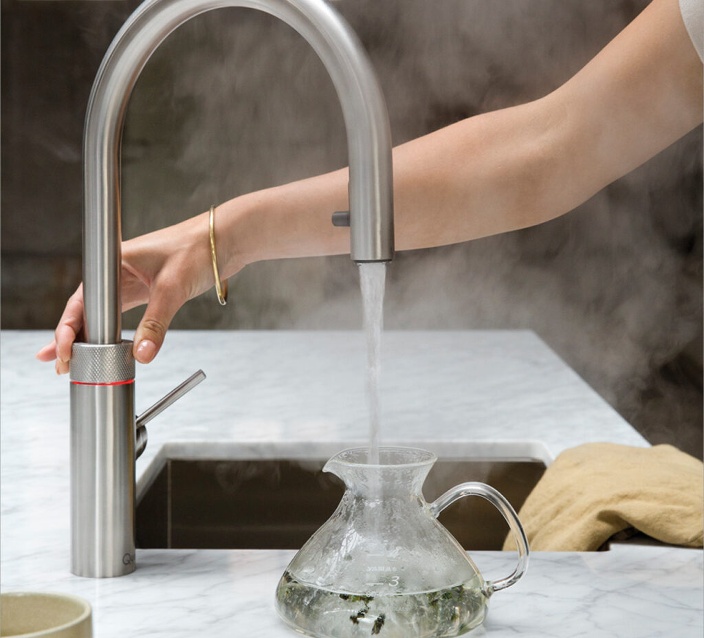 Kochendwasserhahn füllt Glaskanne am Spülbecken, Dampf steigt auf.