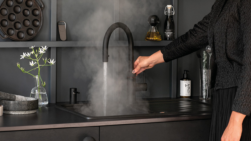 Hand zapft kochendes Wasser am Quooker Hahn, viel Dampf.