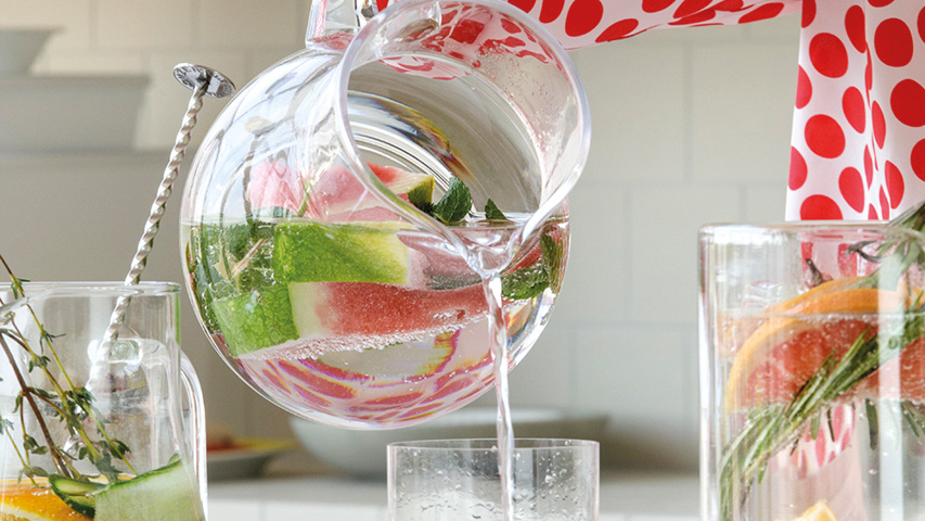 Glaskaraffe mit Wasser, Obst und Minze wird ins Glas gegossen.