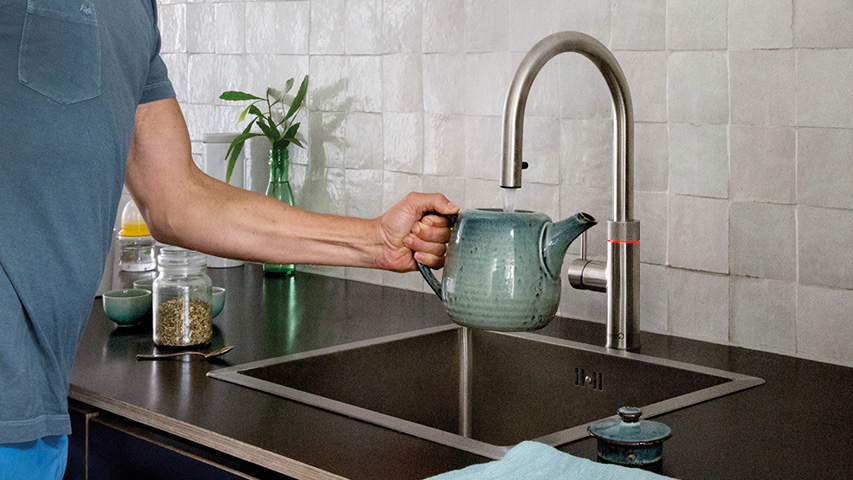 Hand füllt Teekanne am Quooker Wasserhahn über Spülbecken.