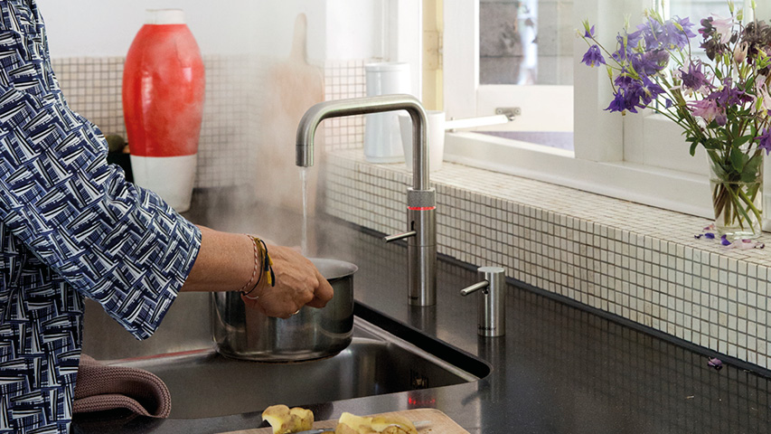 Quooker Wasserhahn füllt Topf am Spülbecken, Dampf steigt auf.
