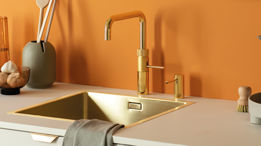 Goldener Quooker Wasserhahn an Spüle in moderner Küchenzeile.
