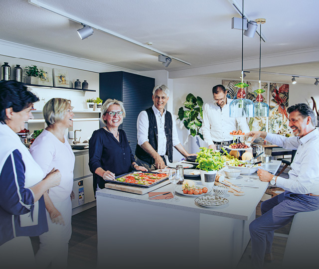 Team in Küchenstudio an Kochinsel im Gespräch, Link zu Über uns