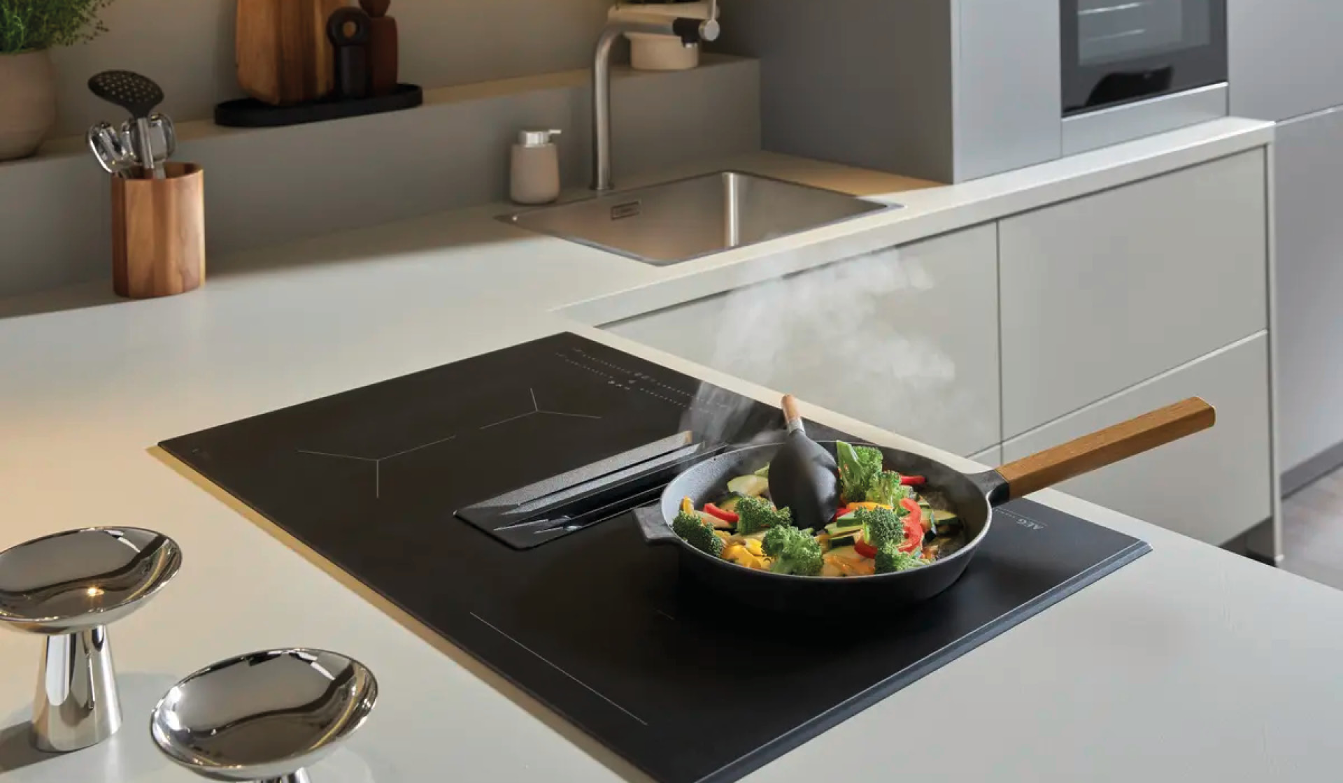 Kochfeld auf Kücheninsel mit Pfanne und dampfendem Gemüse.