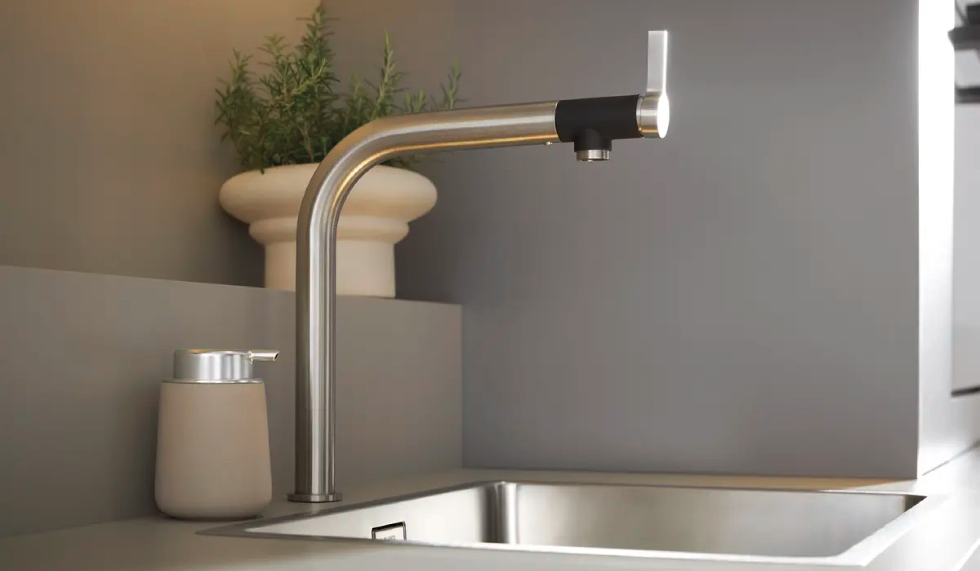 Edelstahl-Armatur über Spülbecken, daneben Seifenspender und Kräutertopf.