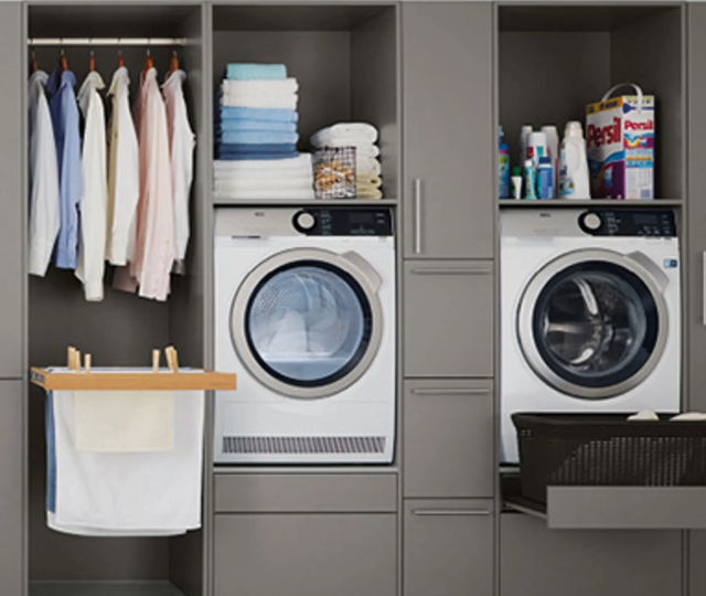 Hauswirtschaftsraum mit Waschmaschine, Trockner, Regalen und Schränken für Kleidung und Haushaltsgeräte. Ordnungssystem für Wäschepflege und Stauraum in modernen Wohnräumen.