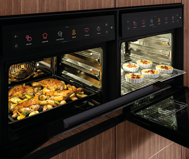 Zwei moderne Einbau Backöfen mit digitaler Bedienung und Innenbeleuchtung. Auf den Blechen befinden sich Ofengerichte und Aufläufe. Hochwertige Küchengeräte für moderne Küchen.